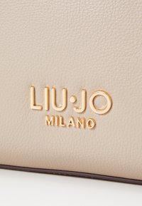 Sac en cuir beige avec marquage en relief doré « LIU·JO MILANO », doté d'une surface texturée et de bords lisses.