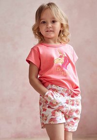 Koralowy t-shirt z krótkim rękawem z grafiką jednorożca, w zestawie z białymi szortami ozdobionymi różowymi wzorami jednorożców, z elastycznym paskiem w talii i kieszeniami.