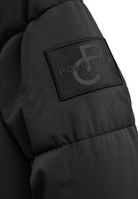 Svart vadderad jackärm med sydd rektangulär svart lapp som visar det präglade "Polo Club"-logotypen.