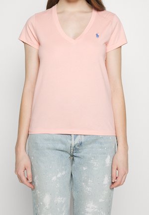 Lys lyserød bomulds t-shirt med v-hals og korte ærmer. Har et lille blåt logo på venstre bryst. Sammen med lyse slidte jeans.