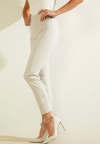 Světle šedé kalhoty s vysokým pasem, úzkého střihu a hladkou texturou, spárované s bílými lodičkami s špičatou špičkou a kotníkovými pásky s kovovými akcenty.