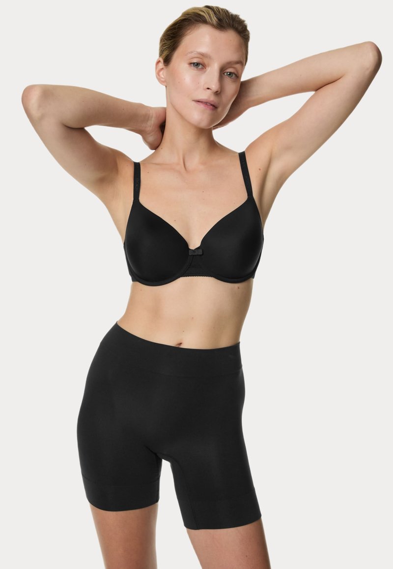 Reggiseno nero senza cuciture con coppe modellate e spalline regolabili, abbinato a pantaloni shapewear neri a vita alta, entrambi realizzati in tessuto liscio.