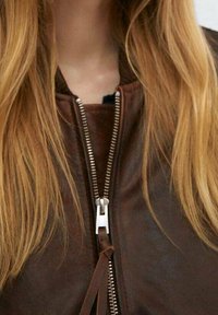 Hnědá kožená bombardovací bunda s vysokým límcem, vybavená stříbrným zipem, jemnými švy a hladkým, strukturovaným povrchem.