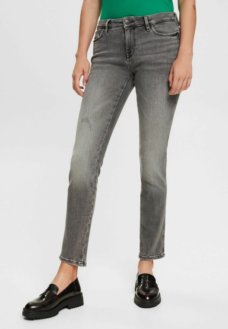 Graue Jeans aus Denim mit schlankem Schnitt, Fünf-Taschen-Design, leichter Abnutzung vorne und mittelhoher Taille. Kombiniert mit schwarzen Loafern.
