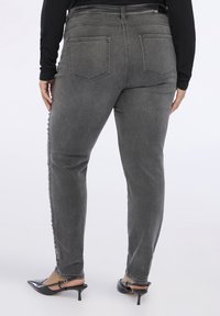 Jeans de mezclilla gris con un corte ajustado, que presentan un hardware decorativo a lo largo del costado, y una cintura de altura media con dos bolsillos traseros.