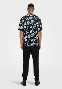 Kurzarmhemd mit navyfarbenem Hintergrund, das mit weißen Blumenmustern verziert ist. Kombiniert mit schwarzen Hosen und schwarzen Schuhen.