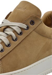 Sneaker in suede marrone chiaro con lacci beige, occhielli in metallo rotondi e suola in gomma bianca. Presenta cuciture sottili e logo impresso sulla linguetta.