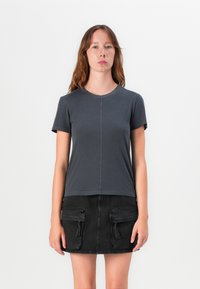 Mörkgrå kortärmad T-shirt med rund halsringning, med synliga sömnadsdetaljer och rak fåll, i kombination med en svart denimkjol.