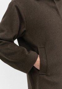 Bruine textuurjasje met een zak, met een losse pasvorm en lange mouwen, gemaakt van een zachte stof in een warme, gedempte tint.