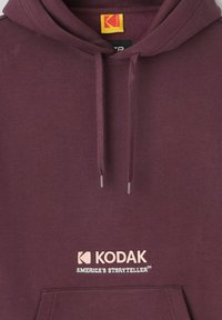 Sweat à capuche bordeaux avec poche avant, cordons de serrage et logo "Kodak America's Storyteller" imprimé en couleurs claires sur la poitrine.