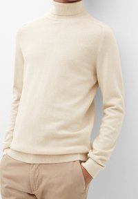 Pull à col roulé crème avec un motif texturé, poignets et ourlet côtelés, associé à un pantalon beige.