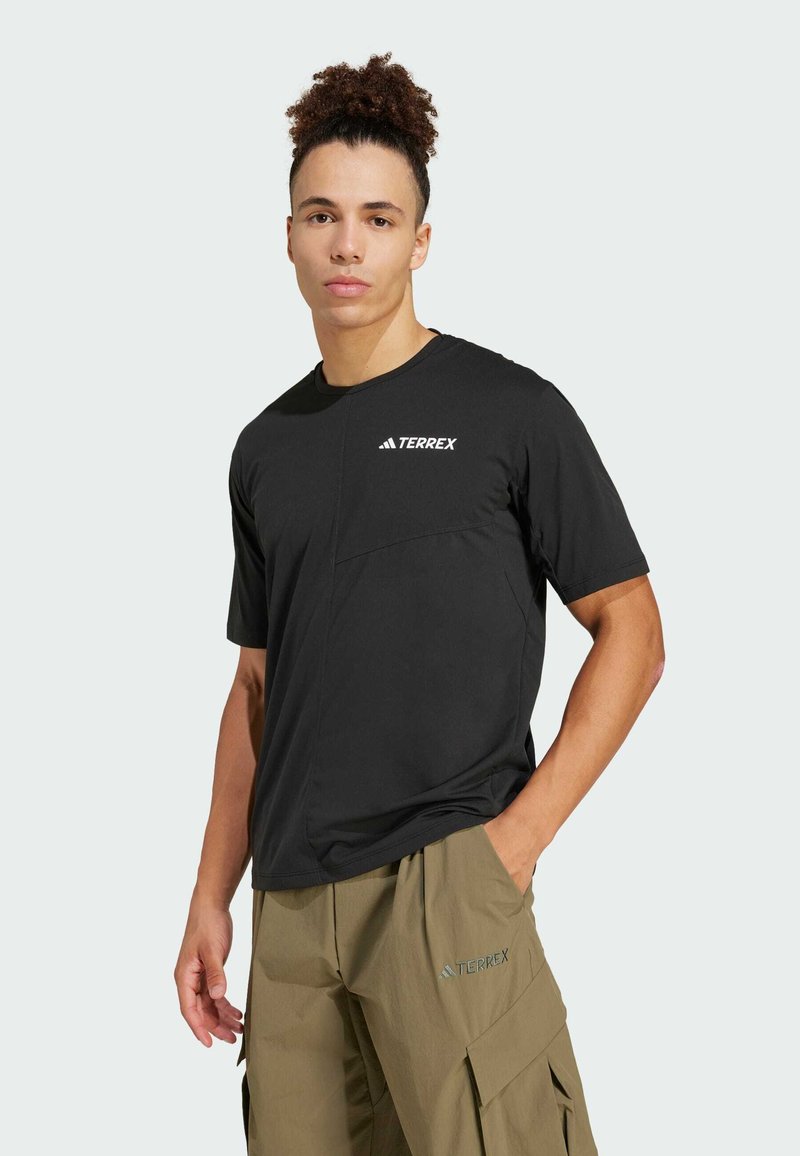 Zwarte T-shirt met korte mouwen en een ritszak, met het witte "TERREX" logo op de linkerschouder, gemaakt van ademende stof. Casual pasvorm.