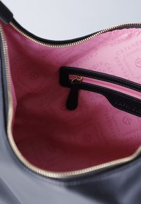 Interno di una borsa nera con fodera rosa caratterizzata da loghi ripetuti. Include una tasca con zip e dettagli in zip dorati.