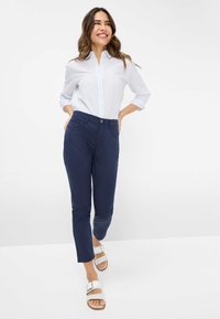 Lichtblauwe en witte gestreepte overhemd met knoopjes, marineblauwe broek en witte sandalen. De broek heeft zijzakken; het overhemd heeft een kraag en opgerolde mouwen.