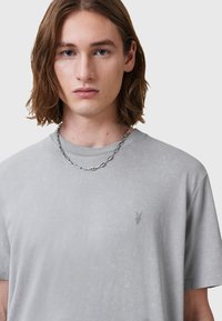 T-shirt in cotone grigio chiaro con maniche corte, caratterizzato da un logo in rilievo sottile sul petto e una finitura liscia e testurizzata.