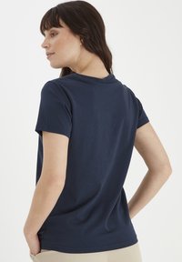 Tricou din bumbac bleumarin, cu mâneci scurte, decolteu rotund și o croială lejeră. Textură netedă cu detalii de design minime.