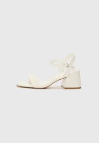 White heeled sandal with a square toe, wide front strap, and adjustable ankle strap. The block heel is textured and slightly wider.