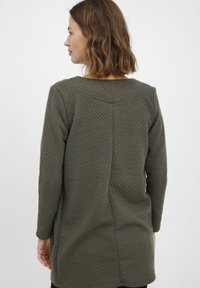 Beige texturerad tröja med långa ärmar, rund krage och en något åtsittande passform. Har synliga sömmar och ett vävt mönster.