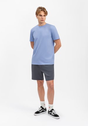 T-shirt bleu clair à manches courtes associé à un short gris foncé. Le modèle porte des baskets noires et des chaussettes à motifs. Design de tenue simple et décontracté.