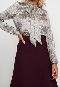 Blusa di seta con motivo leopardato in tonalità di crema e nero, con un fiocco al colletto. Abbinata a una gonna di un viola scuro.