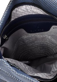 Vnitřek modré texturované tašky s kapsou na zip, šedého podšívkou s opakujícími se textovými vzory a hladkým námořnickým zipem.