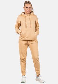 Beige hoodie met een voorzak en trekkoorden, gecombineerd met bijpassende tapered joggingsbroek, voorzien van elastische manchetten en een zachte textuur.