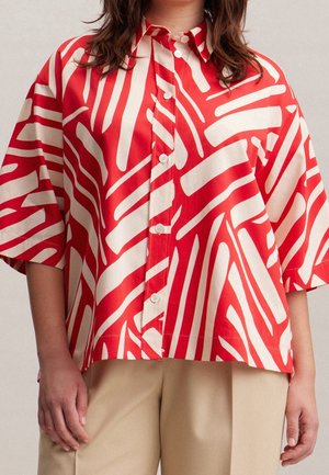 Chemise surdimensionnée rouge et crème à manches courtes, présentant un motif à rayures abstraites audacieuses, fabriquée en coton léger.