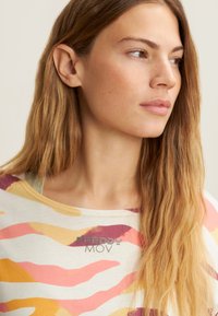T-shirt leggero con motivo in beige tenue e onde audaci in rosa, giallo e viola. Presenta il logo "FREDDY MOV" sul petto.