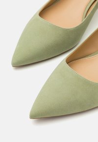Ballerine a punta in morbido suede verde tenue, con un interno liscio e dettagli di cucitura minimal lungo l'apertura.