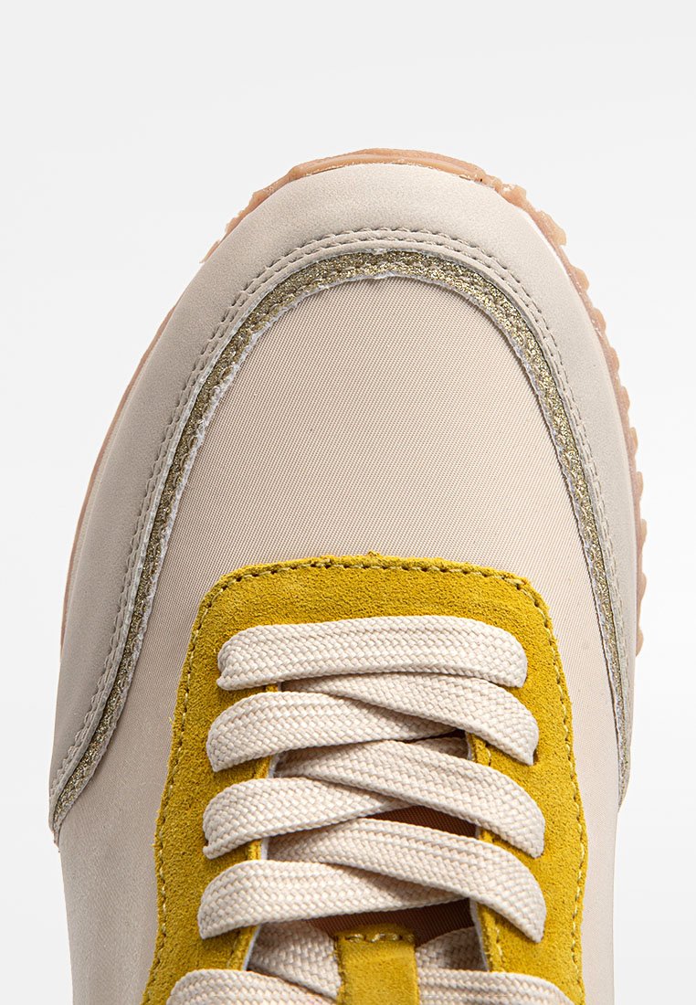 Beige Sneaker mit gelben Nubukakzenten, metallischen goldenen Details entlang der Kante und cremefarbenen Schnürsenkeln. Obermaterial aus strukturiertem Stoff und Gummisohle.