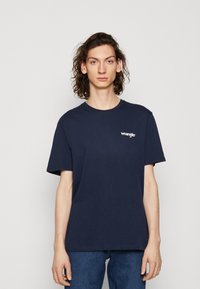 Námorníckomodrá bavlnená tričko s krátkymi rukávmi a okrúhlym výstrihom, s bielym logom "Wrangler" na ľavej hrudi.
