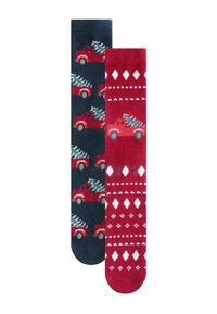 Dos pares de calcetines: uno azul marino con camiones rojos que llevan árboles de Navidad, el otro rojo con patrones de diamantes y árboles en blanco. Textura de punto.