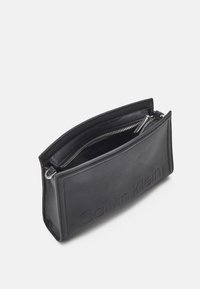 Pochette in pelle nera con logo in rilievo, chiusura con zip superiore e superficie liscia. Forma rettangolare compatta, caratterizzata da un design sottile e minimalista.