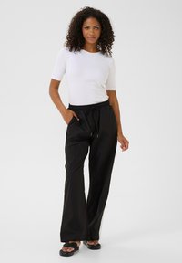 Zwarte, losse broek met een elastische tailleband en zijzakken. Gecombineerd met een witte, aansluitende, geribbelde top met korte mouwen.