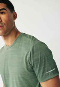 Grøn atletisk t-shirt med struktureret stof, rund halsudskæring og korte ærmer. Har en reflekterende detalje på venstre ærme.