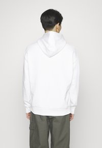 Witte hoodie met een ontspannen pasvorm, ribgebreide manchetten en zoom. Zacht materiaal, zichtbare stiksels en een enkele naad op de rug.