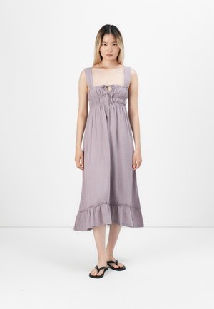 Lavendelkleurige midi-jurk met een nauwsluitend lijfje, brede bandjes en een gerimpelde zoom. Voorzien van smocking en een strikdetail aan de voorkant. Gedragen met zwarte flip-flops.