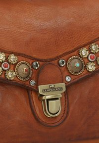 Borsa in pelle marrone con superficie testurizzata, chiusura in metallo dorato e decorazioni impreziosite da pietre colorate e accenti metallici.