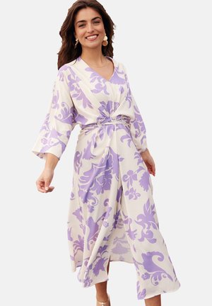 Robe longue couleur crème avec des motifs floraux violets, présentant un décolleté en V, des manches larges, une ceinture à la taille et une silhouette fluide.