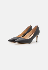 Zwarte leren hoge hakken met een puntige neus, slanke stiletto-hak en tan binnenvoering. Gladde textuur zonder patronen.
