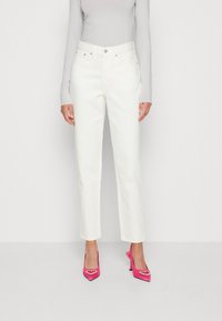 Vita raka jeans med hög midja, femfickorsdesign och knappstängning, i kombination med rosa spetsiga klackar med hjärtdetaljer.