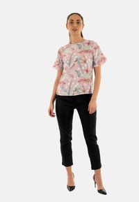 Blusa floreale a maniche corte di colore rosa con dettagli blu e bianchi, abbinata a pantaloni neri slim-fit. La modella indossa tacchi alti neri.