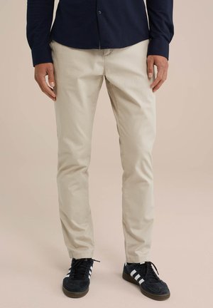 Beige pamut chinos egyenes fitettel, sima textúrával és oldalsó zsebekkel, fekete sportcipővel és sötét inggel párosítva.