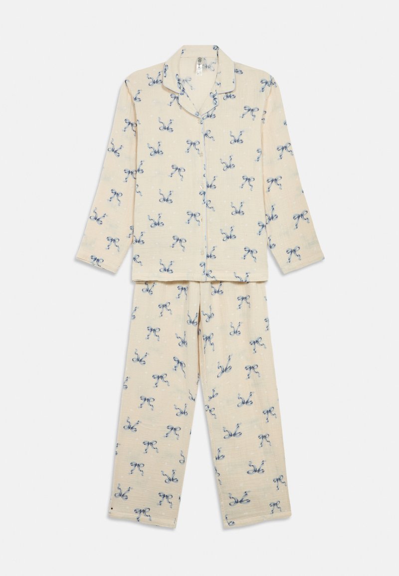 Krämfärgad långärmad pyjamashirt med knappar och matchande byxor med små blå rosettmönster överallt.