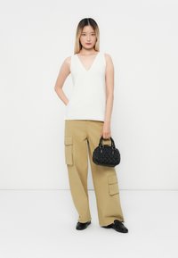 White sleeveless top with a V-neck, paired with khaki wide-leg cargo pants featuring multiple pockets, and a small black textured handbag.