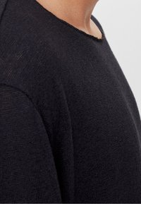 Czarny dziany sweter z luźnym dekoltem, wykonany z teksturowanej tkaniny z wykończeniem bez obrębu, podkreślający jego casualowy design.