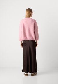 Maglione fuzzy rosa con maniche a palloncino, abbinato a una lunga gonna in satin marrone. Calzature comprendono sneakers marroni con dettagli bianchi.