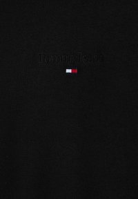 T-shirt in tessuto nero con ricamo della scritta "Tommy Jeans" e un piccolo logo rettangolare rosso, bianco e blu. Texture liscia.