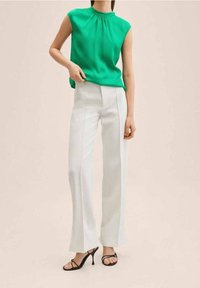 Top sin mangas verde con escote fruncido, combinado con pantalones de pierna ancha blancos y sandalias de tacón alto negras. Diseño sencillo y moderno.