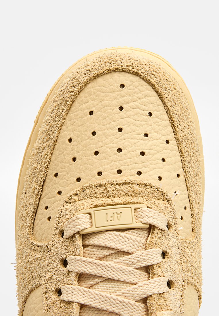 Baskets beiges avec un dessus en daim texturé et une coque en cuir lisse, dotées de perforations, de lacets ronds et d'une étiquette de langue cousue.